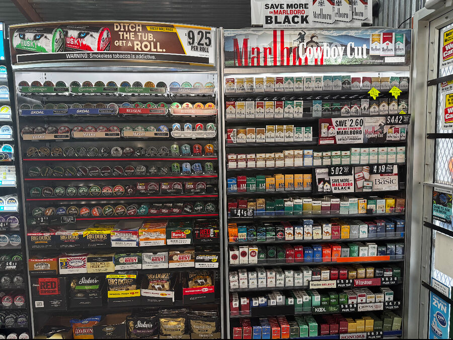 Wall of cigarette packs beside racks of smokeless tobacco tins at Duke's Tobacco